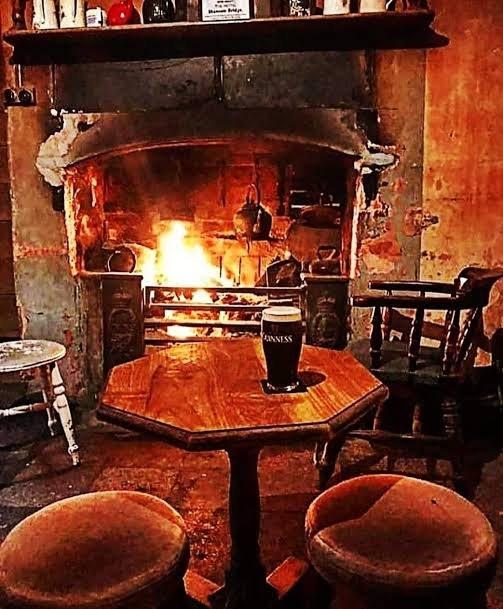 A pint of Guinness on a small wooden table before an open fire in a pub snug